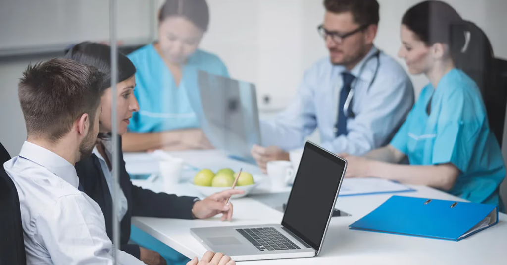 Equipe médica reunida em mesa de trabalho com notebooks